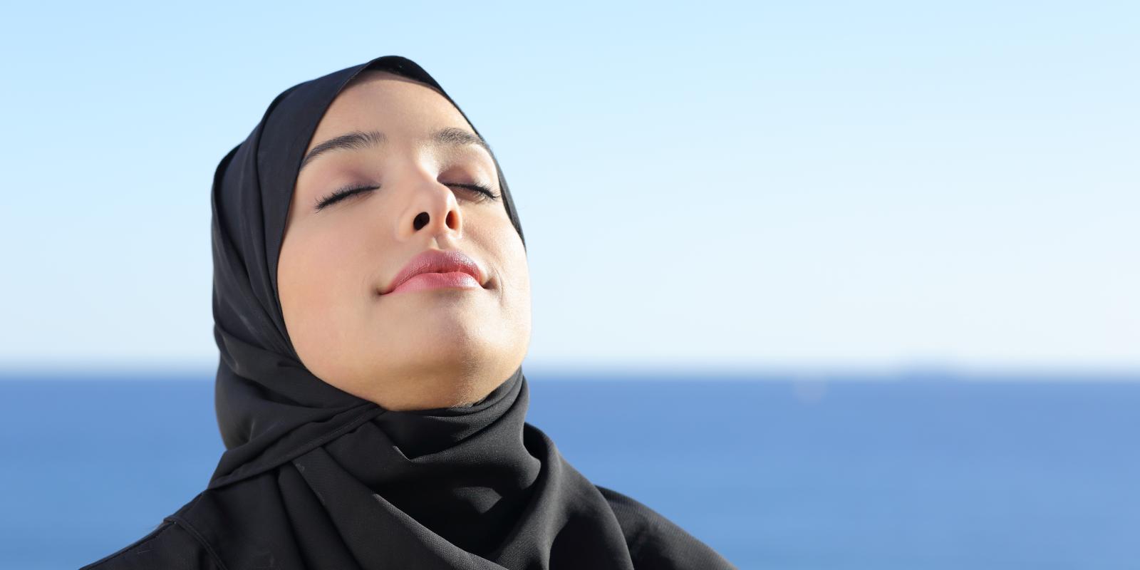 Bilde av kvinne i hijab som gjør pusteøvelse med hav i bakgrunnen.