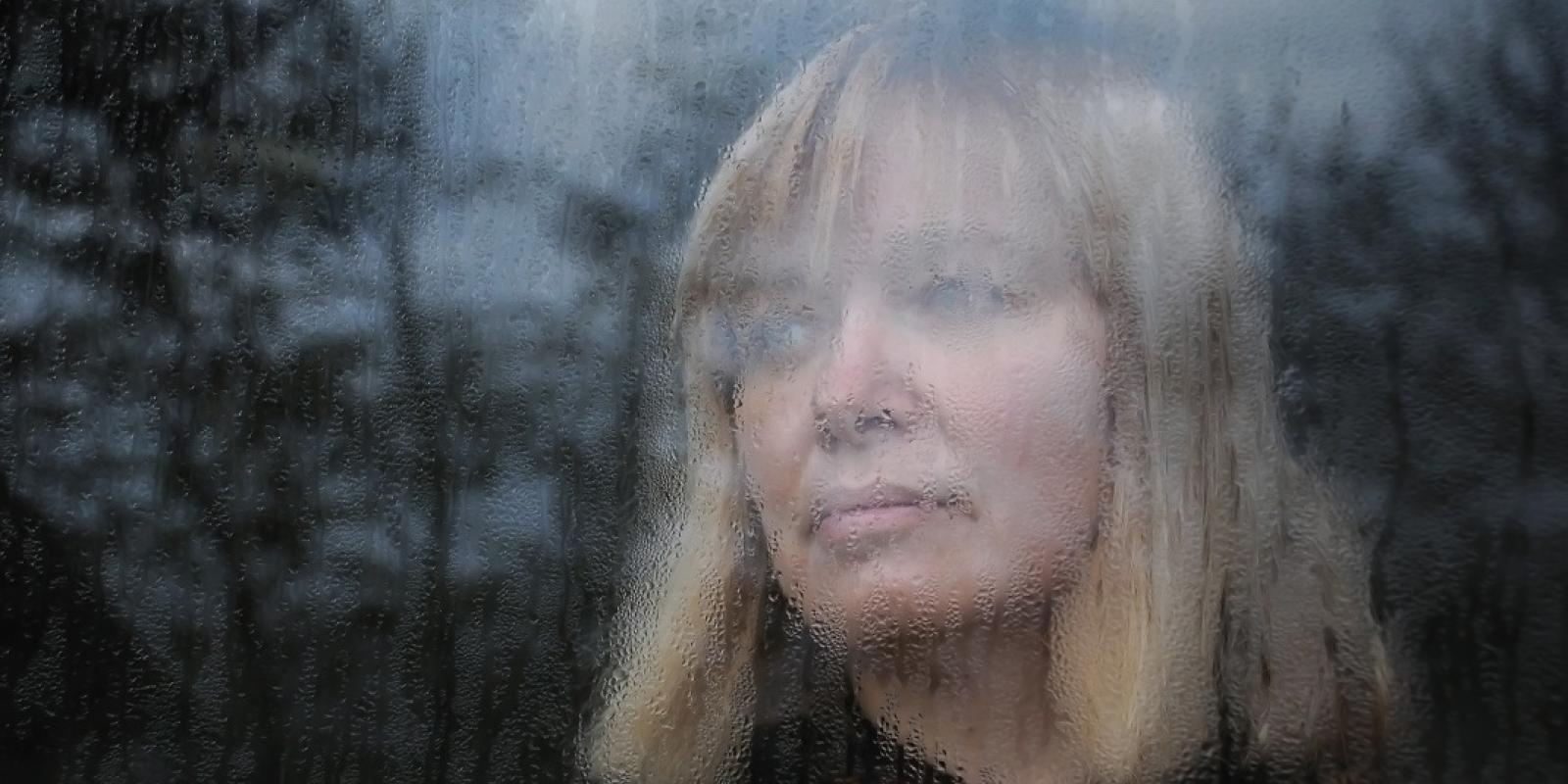 Kvinne bak vindu med regndråper
