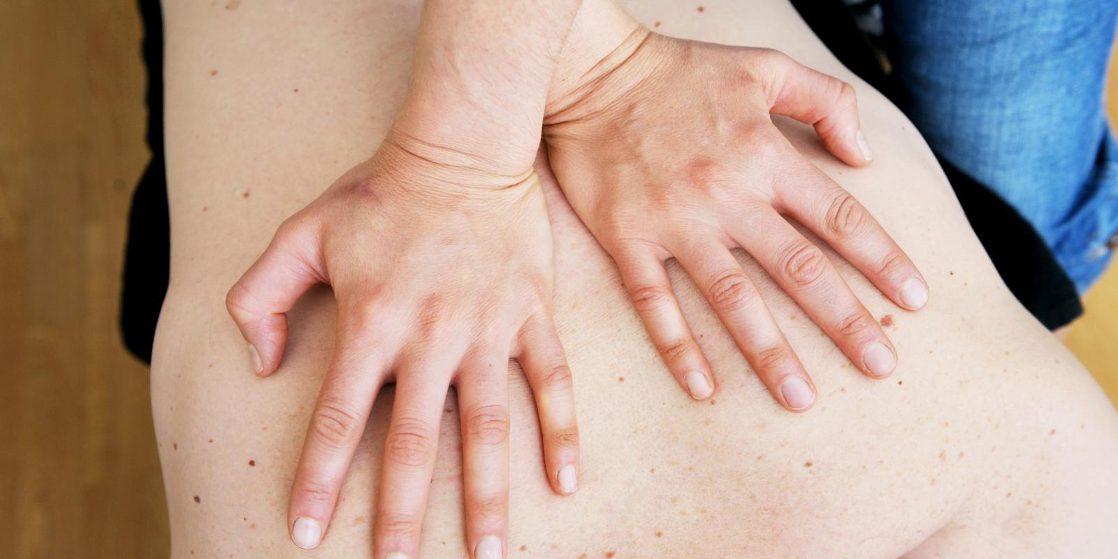 Naprapat trykker hender mot pasientens rygg.