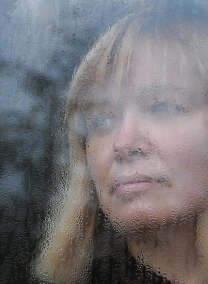 Kvinne bak vindu med regndråper